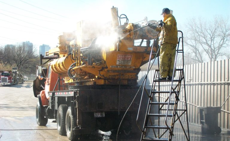 Service professional pressure washing large construction equipment.
